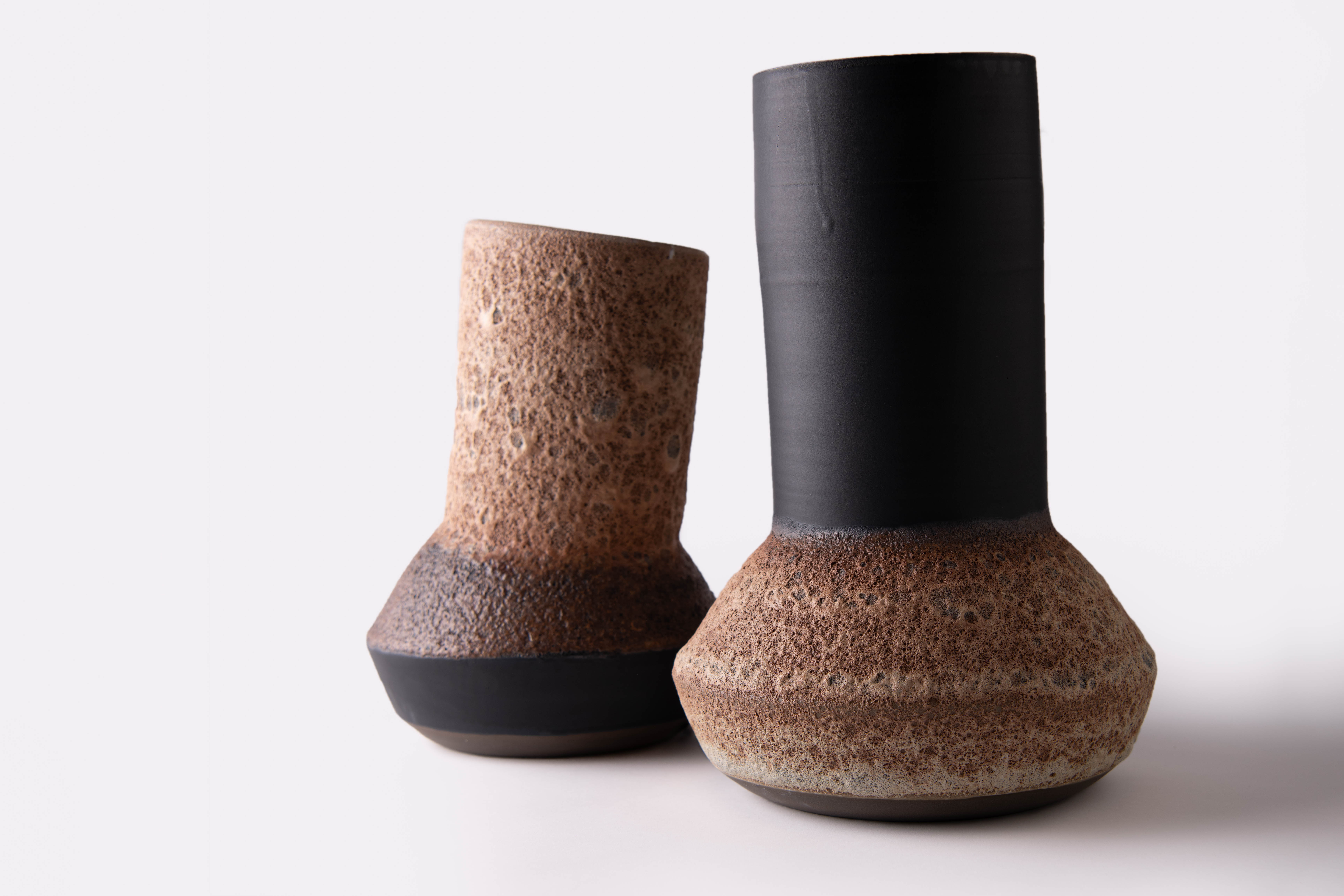Pair of tall asymmetrical ceramic vessels combining dark clay with textured brown surfaces