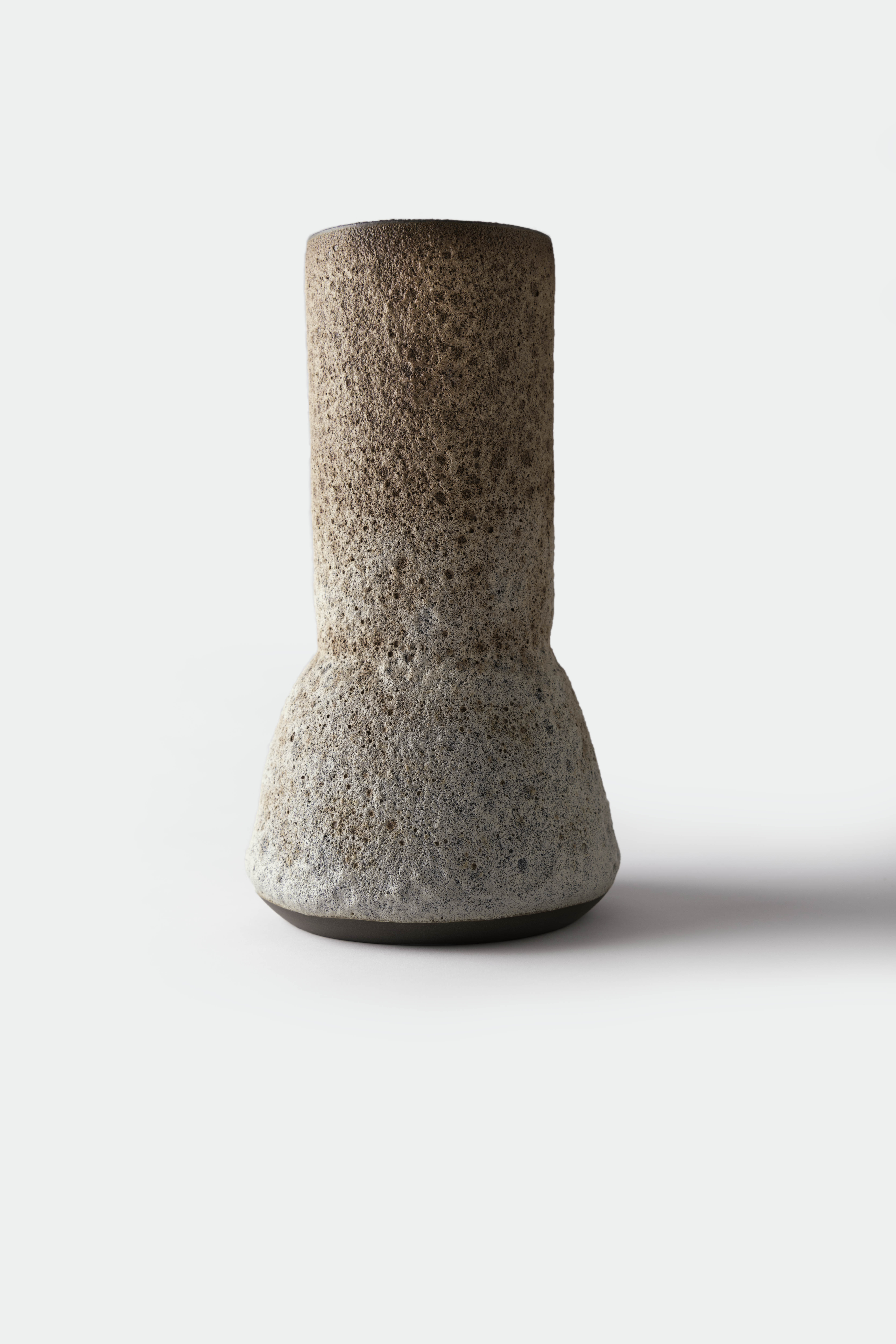 Tall lopsided ceramic vessel with a pale brown volcanic surface