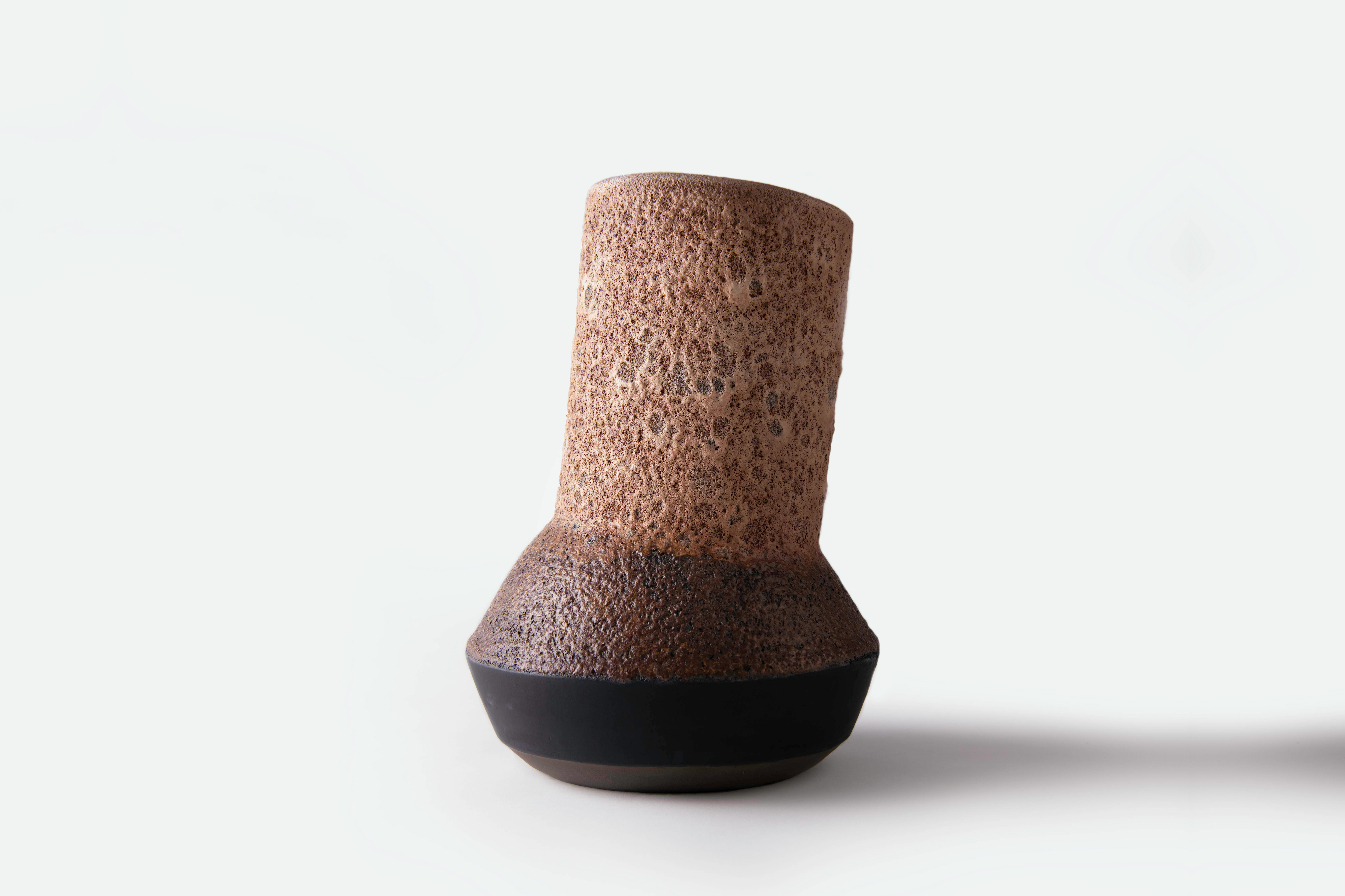 Tall leaning ceramic vessel with a textured brown surface and dark base