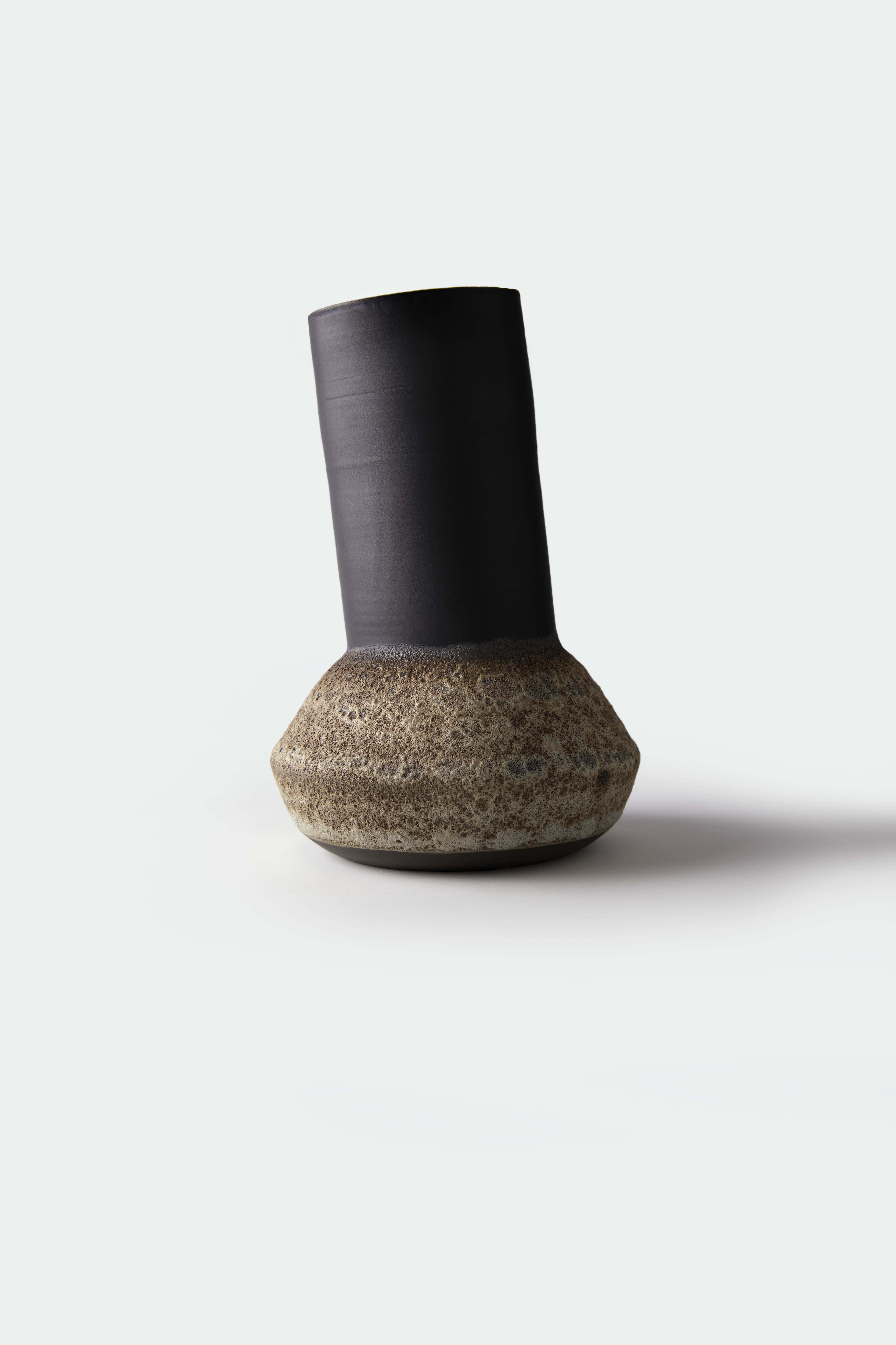 Tall asymmetrical ceramic vessel combining a dark neck with a rounded textured base