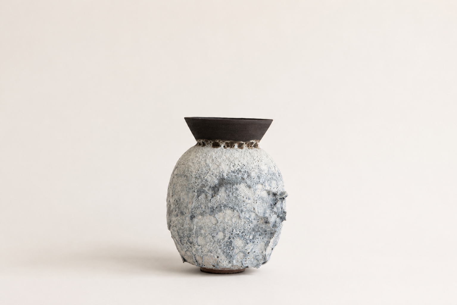 Pale sculptural vessel with an irregular volcanic surface and flared dark rim