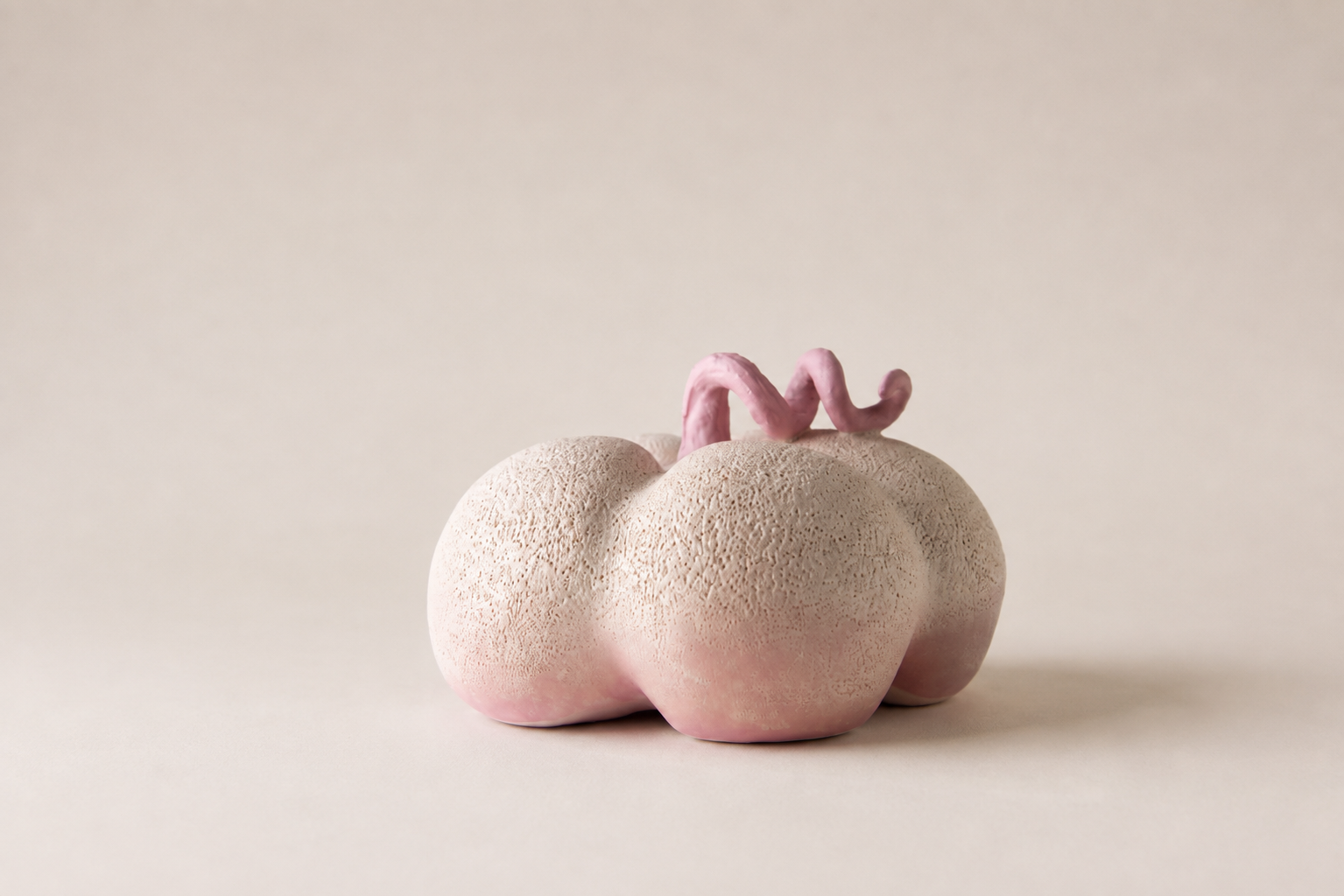 Rounded pale sculptural vessel with a pink base and curling pink detail