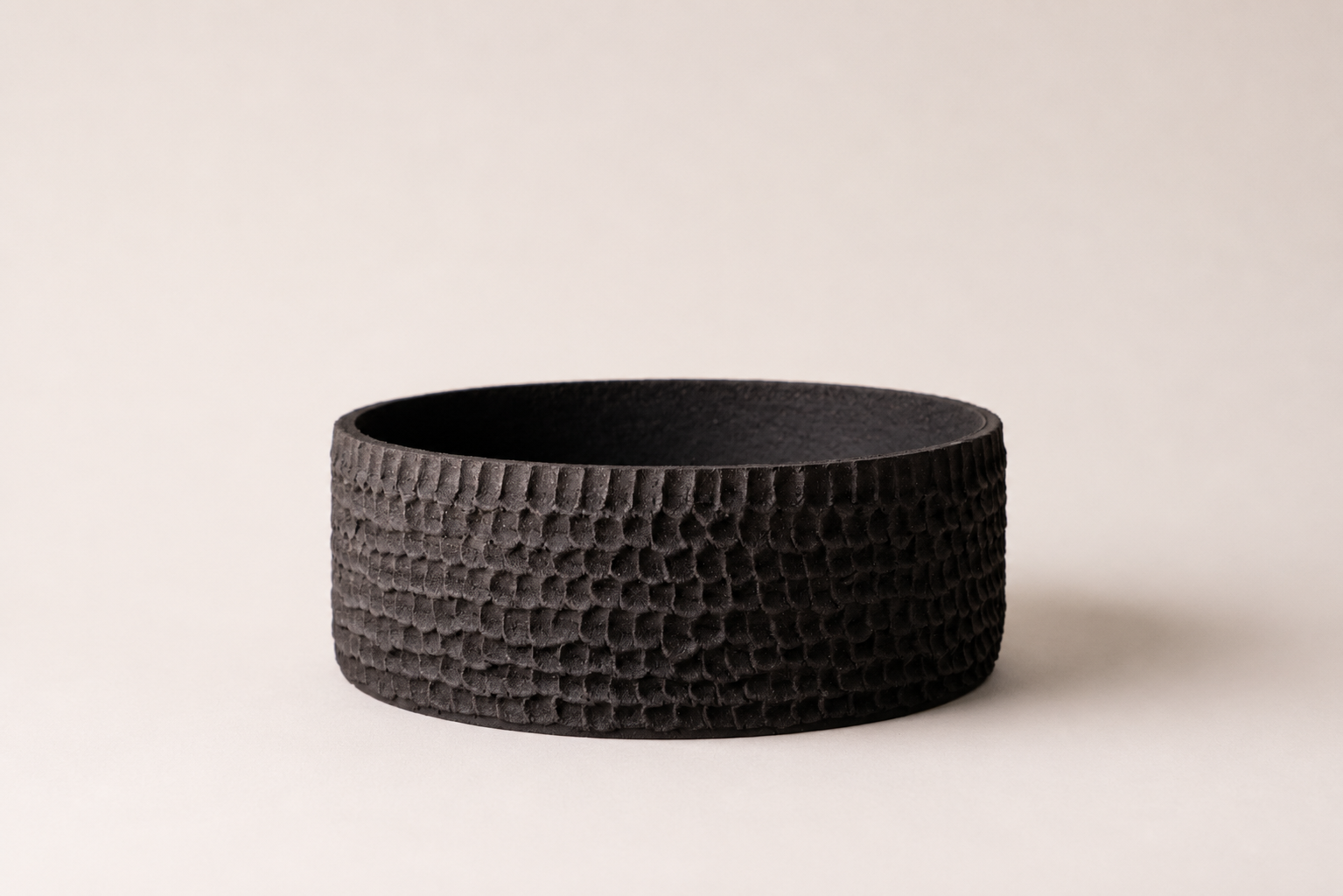 Low black ceramic vessel with a carved rhythmic surface
