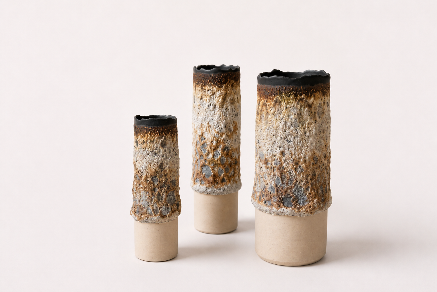 Group of three tall cylindrical vessels with cream, brown and charcoal volcanic surfaces