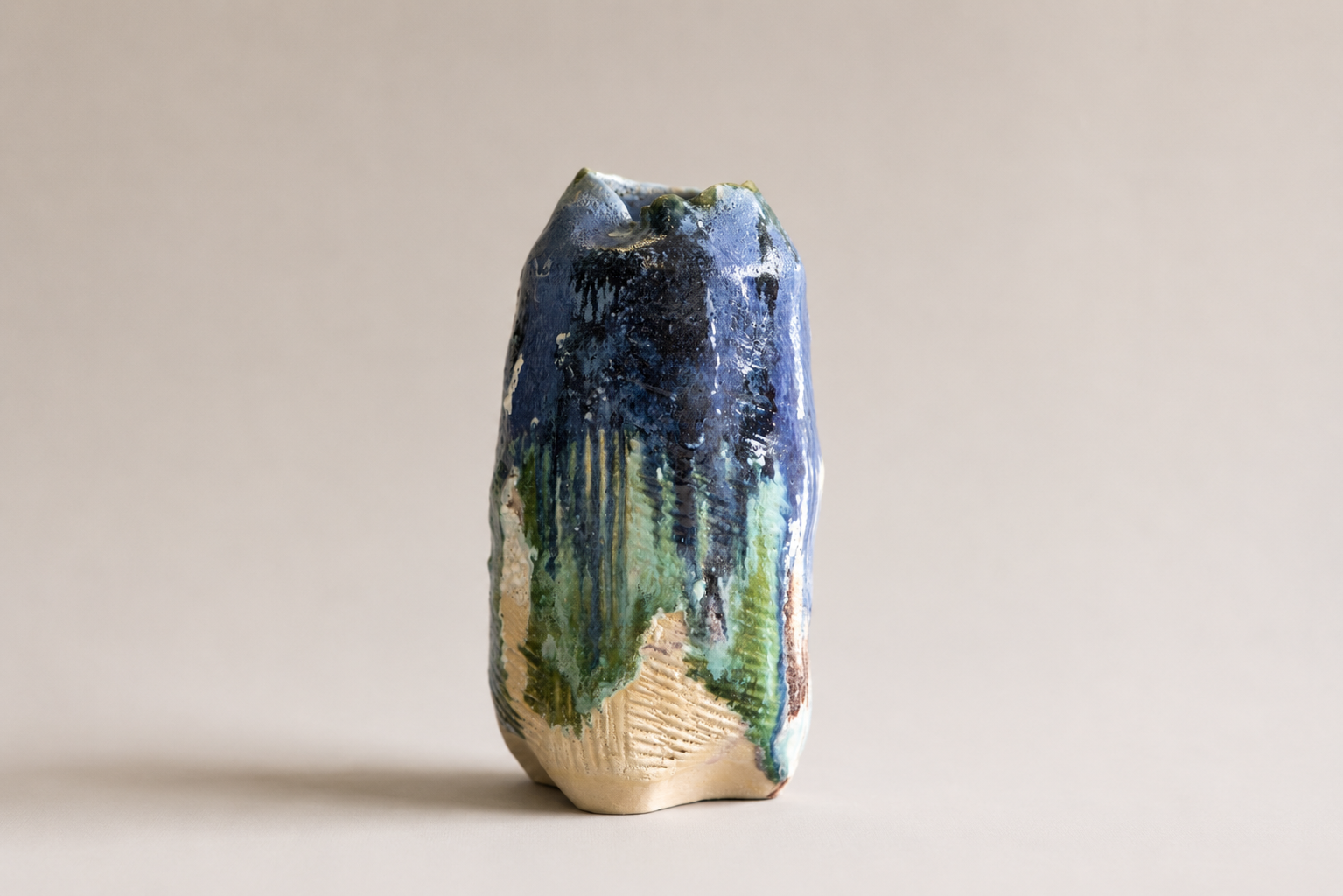 Tall irregular ceramic vessel with layered blue, green and natural clay surfaces