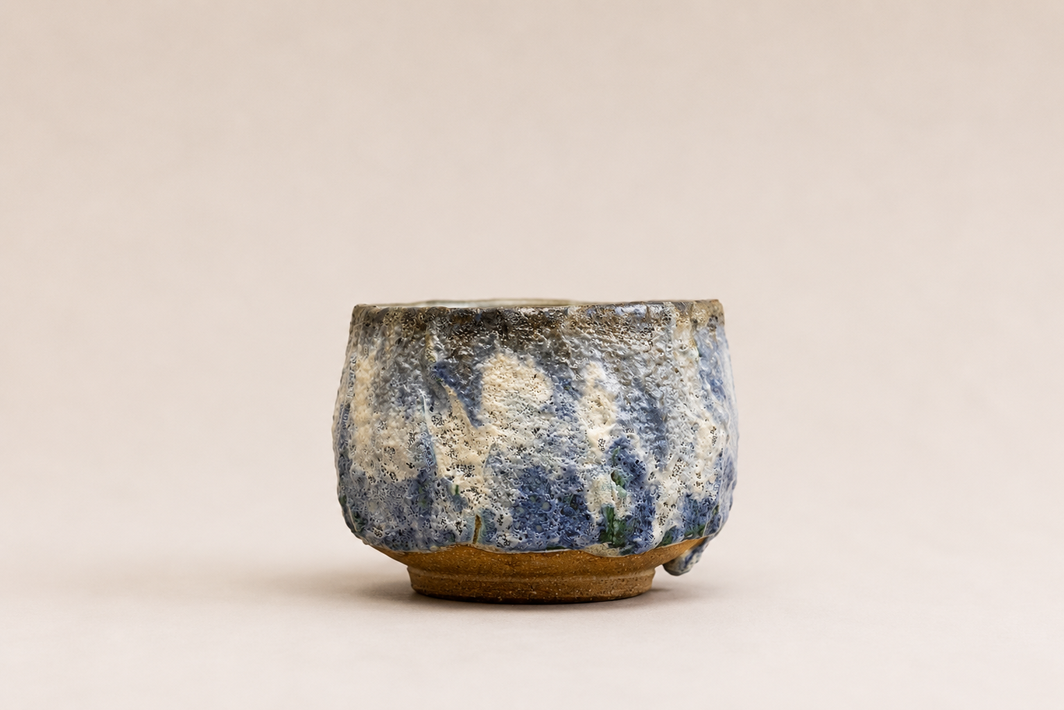 Small rounded ceramic vessel with layered blue, cream and natural clay glazes