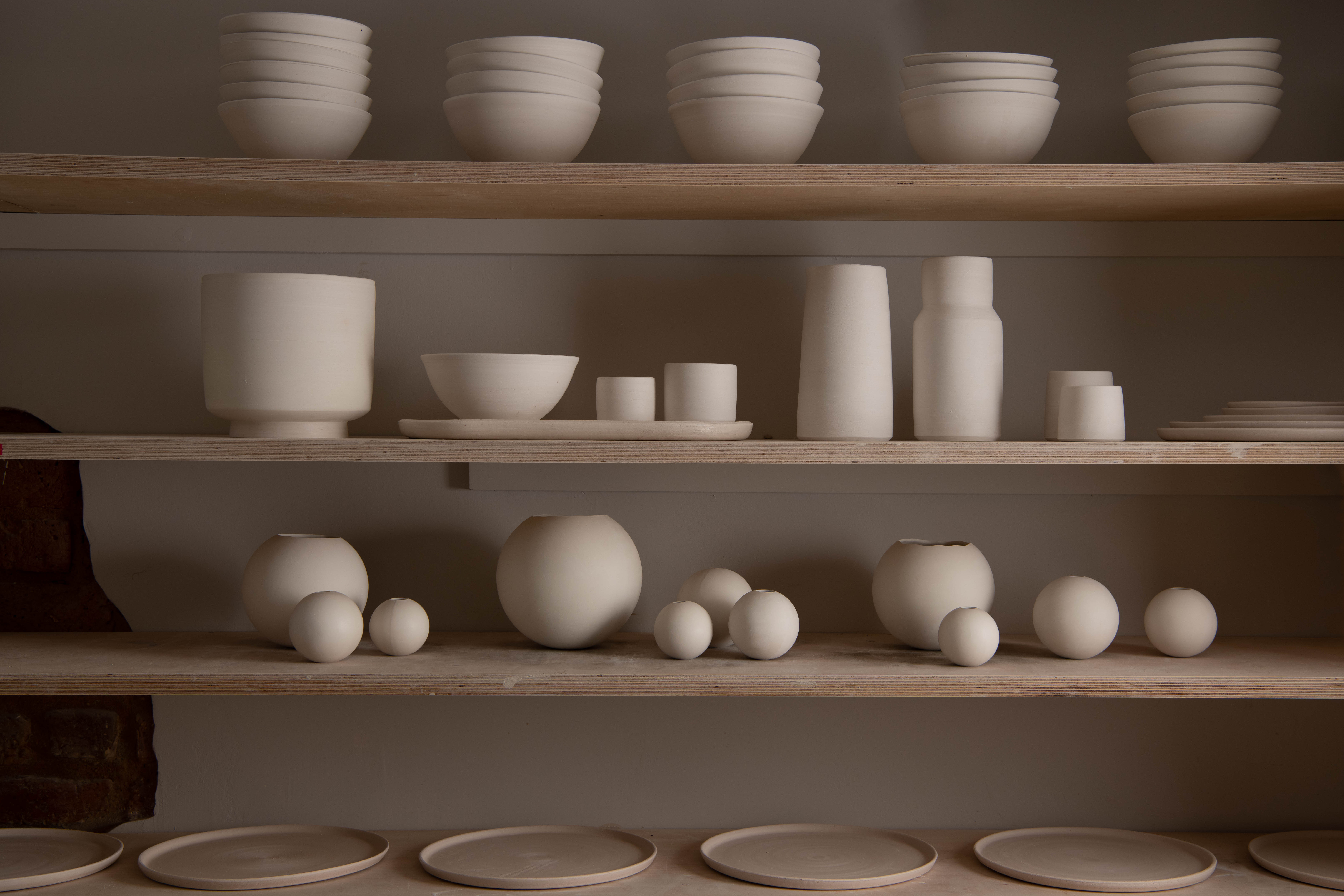 Unfired ceramic bowls, vessels and sculptural forms arranged on studio shelves