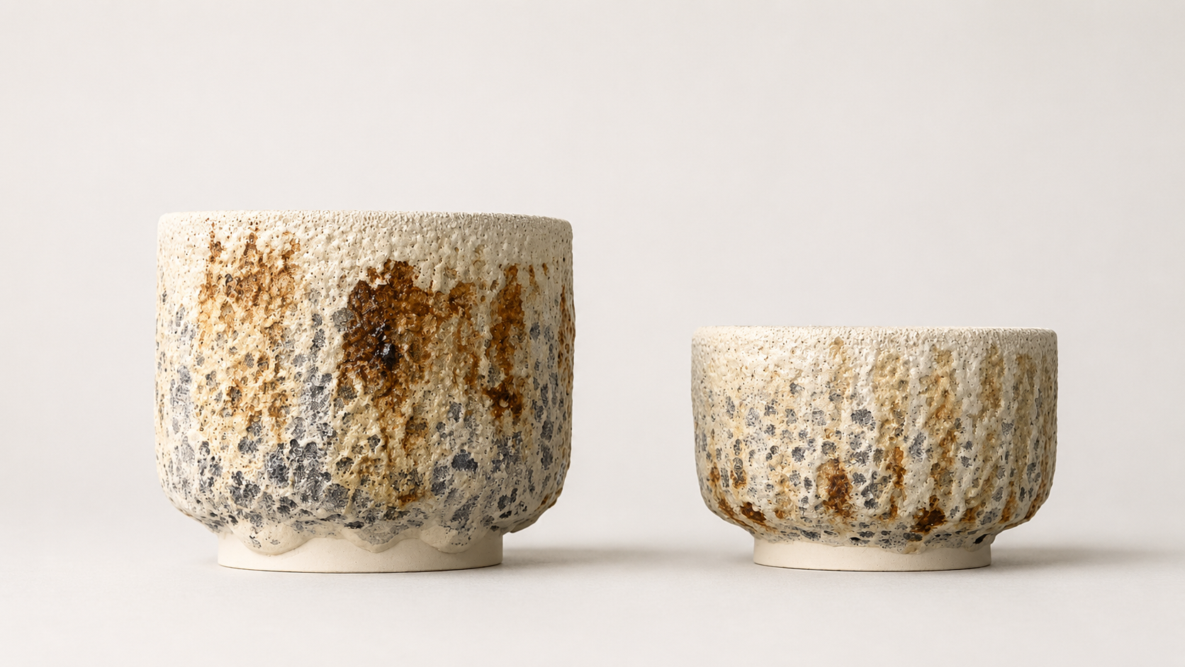 Pair of cylindrical vessels with cream, grey and ochre volcanic surfaces